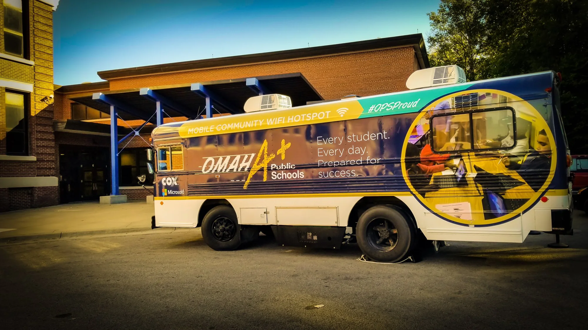 The Omaha Public Schools bus wrapped as a "Mobile Community WiFi Hotspot," with Cox and Microsoft logos and "Every student. Every day. Prepared for success."