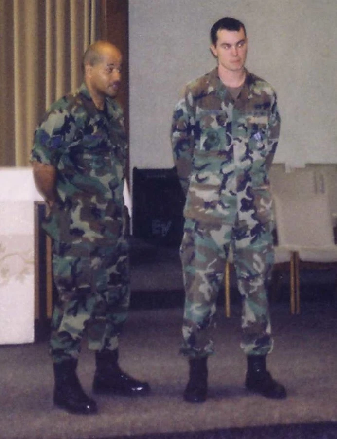 Two airmen in woodland BDUs standing side by side in a briefing room