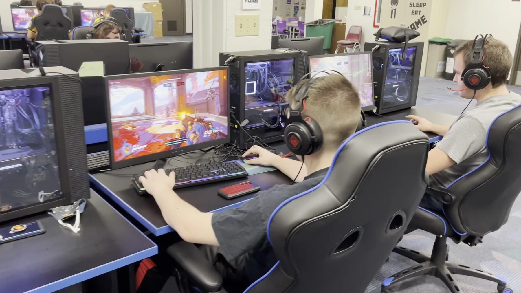 Two students wearing headsets play Overwatch at adjacent Wichita Public Schools esports stations